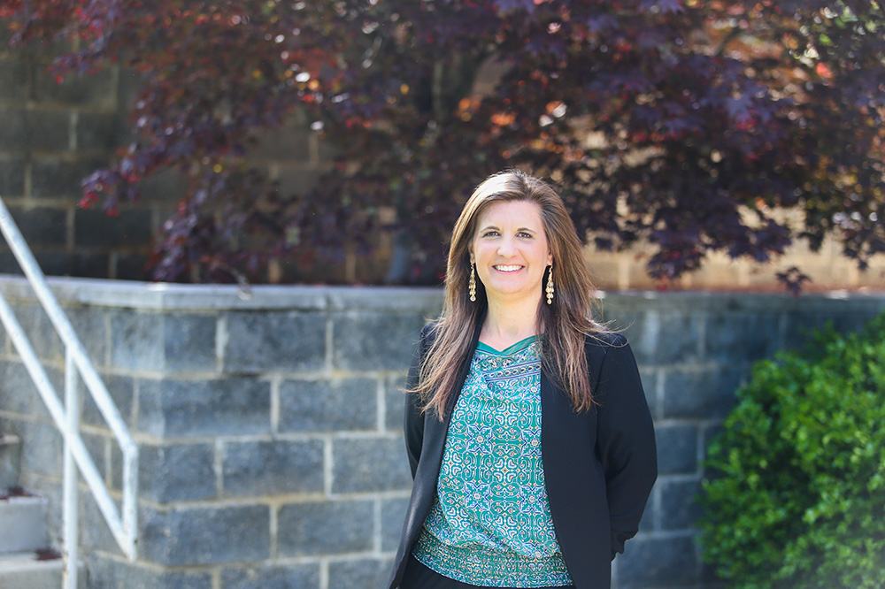 Woman in blazer stands outside, smiling