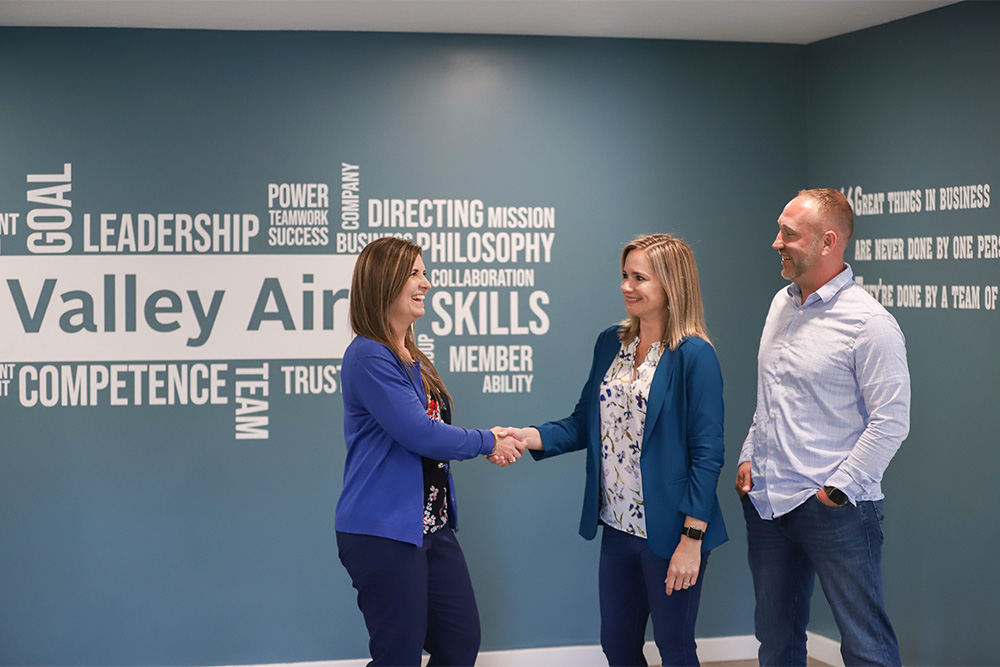 Woman shakes hands with another woman and a man smiles beside them