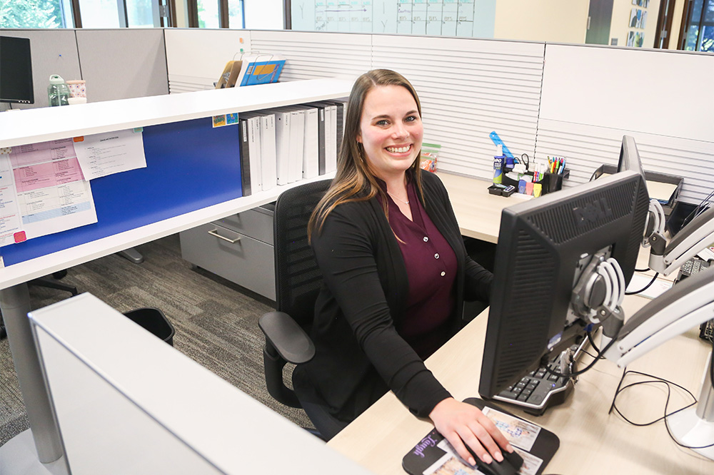 Woman DCCU employee sits at computer, smiling at the camera