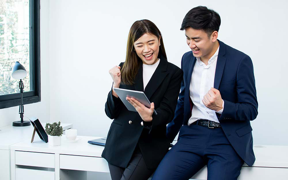 Man and woman smiling at an electronic tablet, excitedly